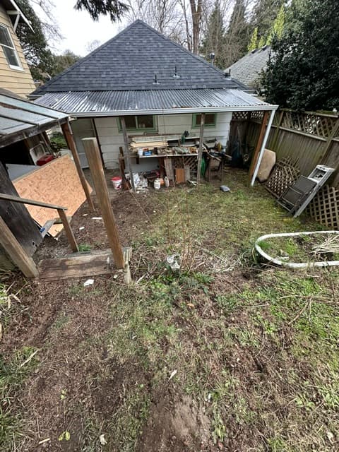 White building with a corrugated metal awning over a cluttered workbench in a backyard.