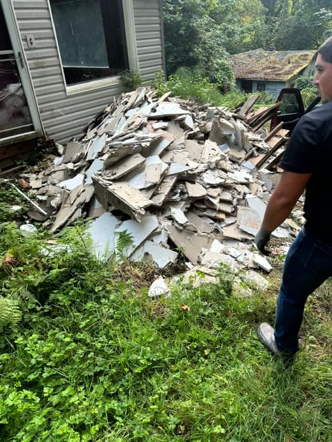 Large pile of broken drywall and construction debris outside a house with a man nearby.